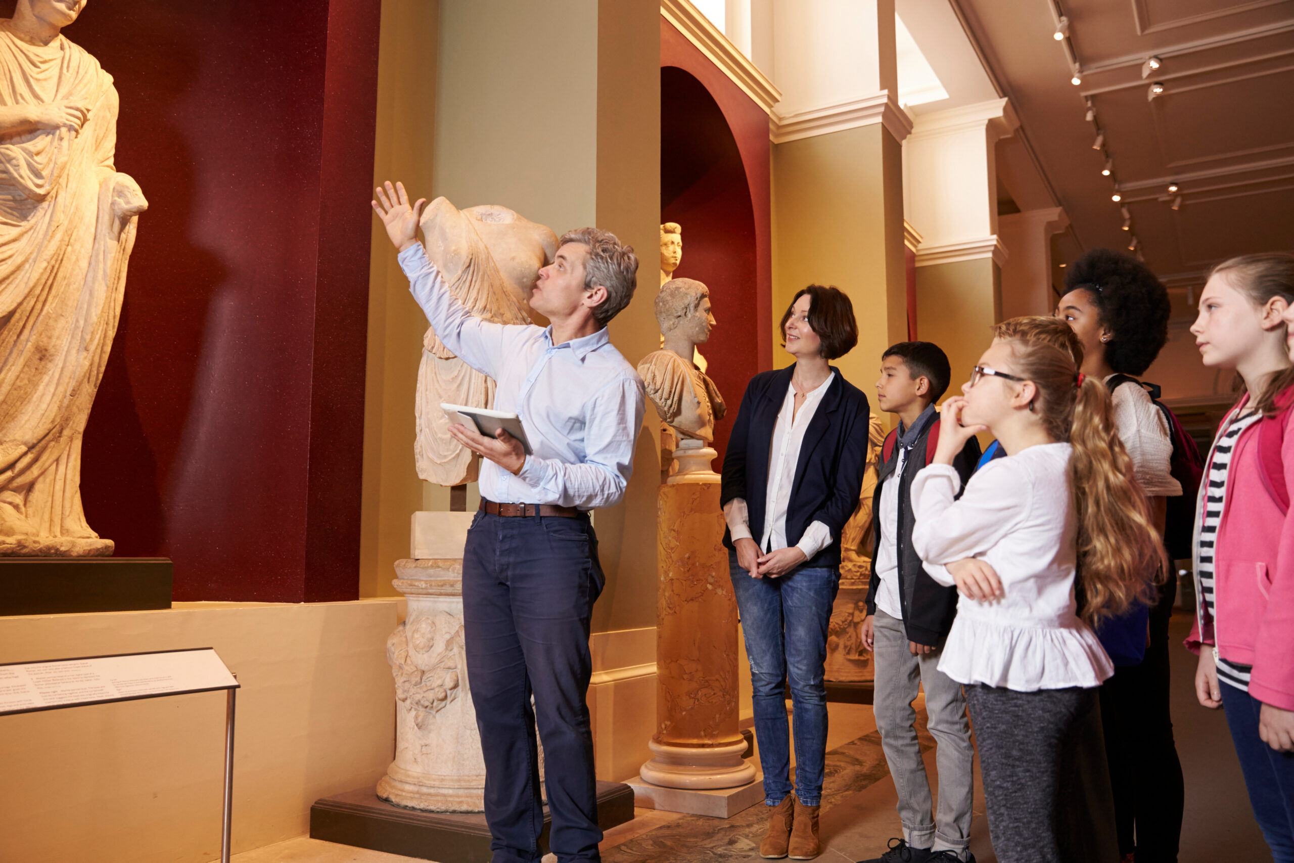 guide in a museum points at a statue while people around him look on